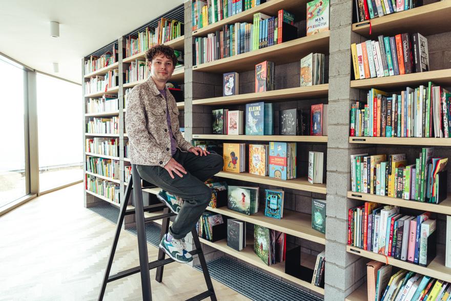 Recensent Bas Maliepaard zit op een trapladder en kijkt naar de boekenkast