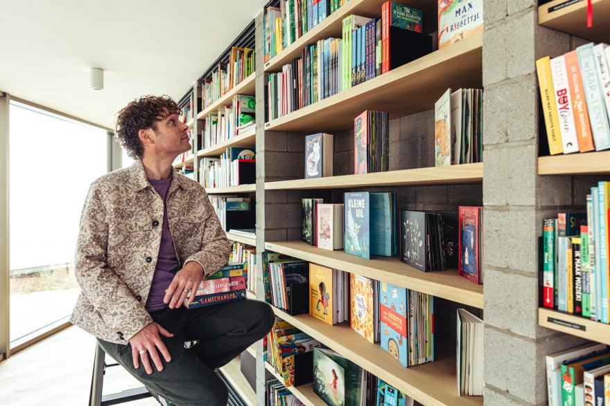 Recensent Bas Maliepaard zit op een trapladder en kijkt naar de boekenkast