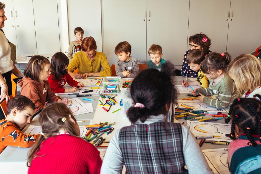 de juryleden van groep 1 werken aan een grote tafel met kleurkrijtjes en kleurplaten