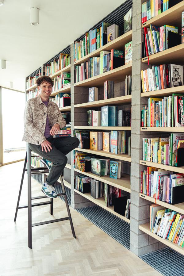 recensent Bas Maliepaard zit op een trapladder voor een boekenkast