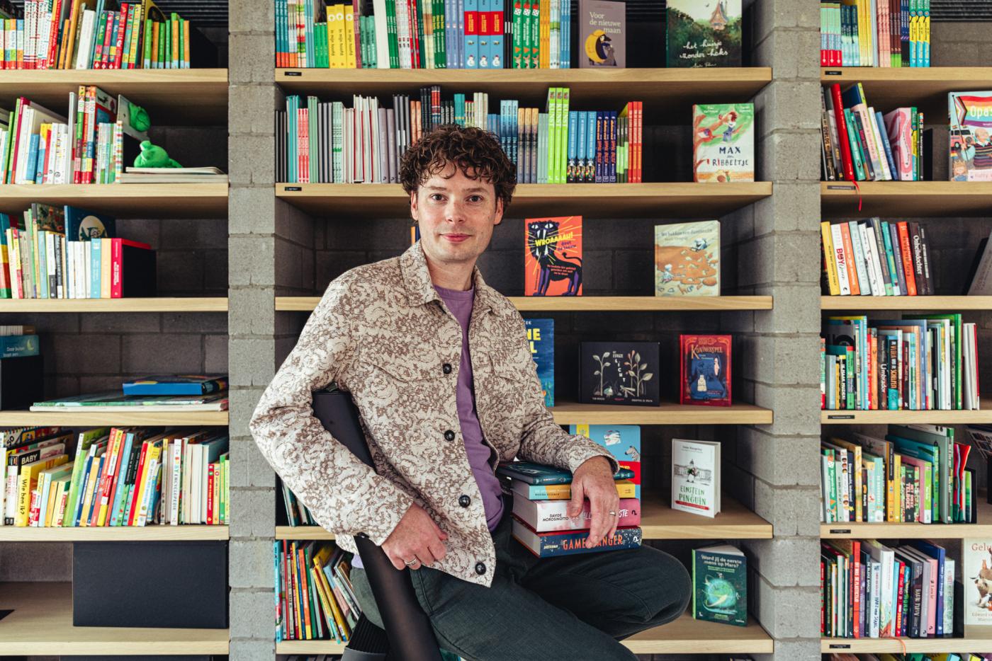 recensent Bas Maliepaard zit voor een boekenkast en kijkt vrolijk in de lens